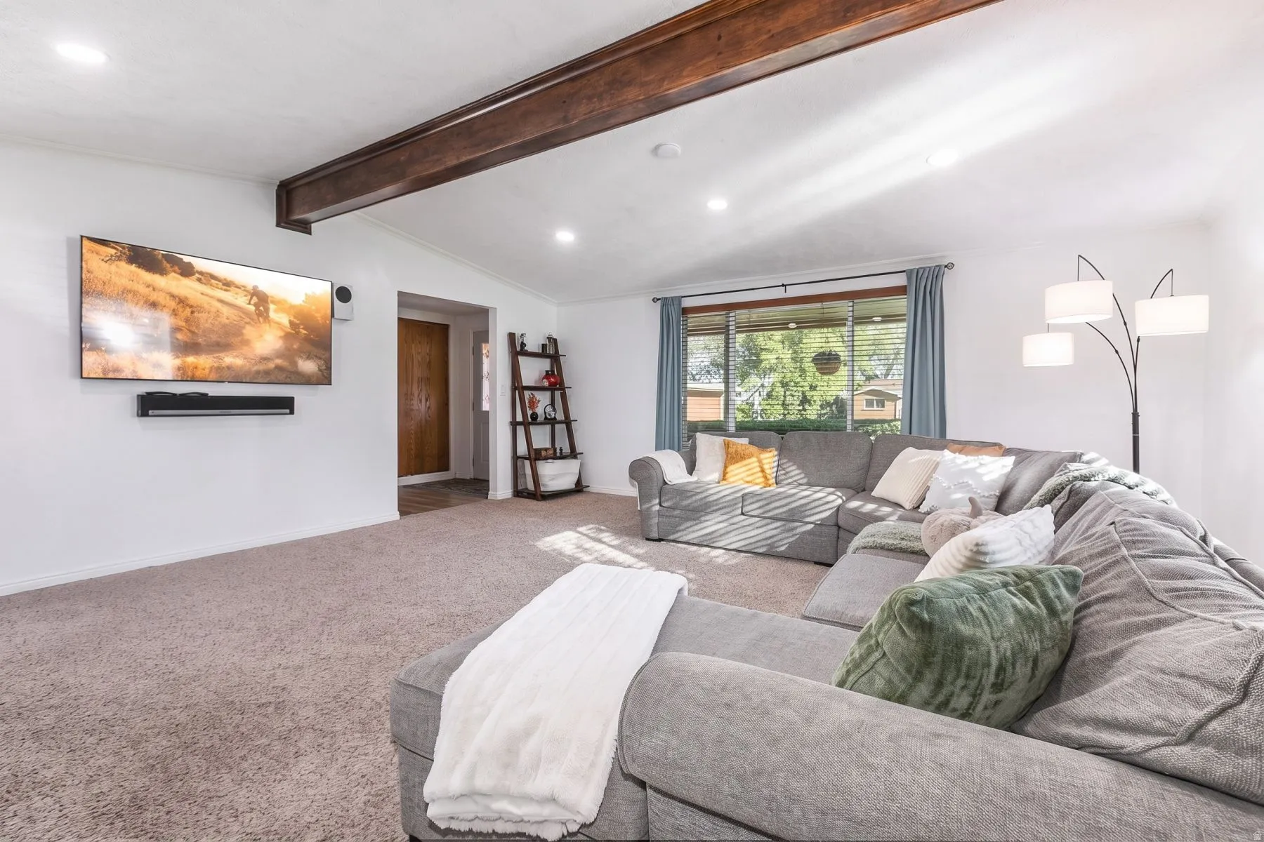 Vaulted ceiling with exposed wood beam, recessed lighting, and a large window with blue drapes