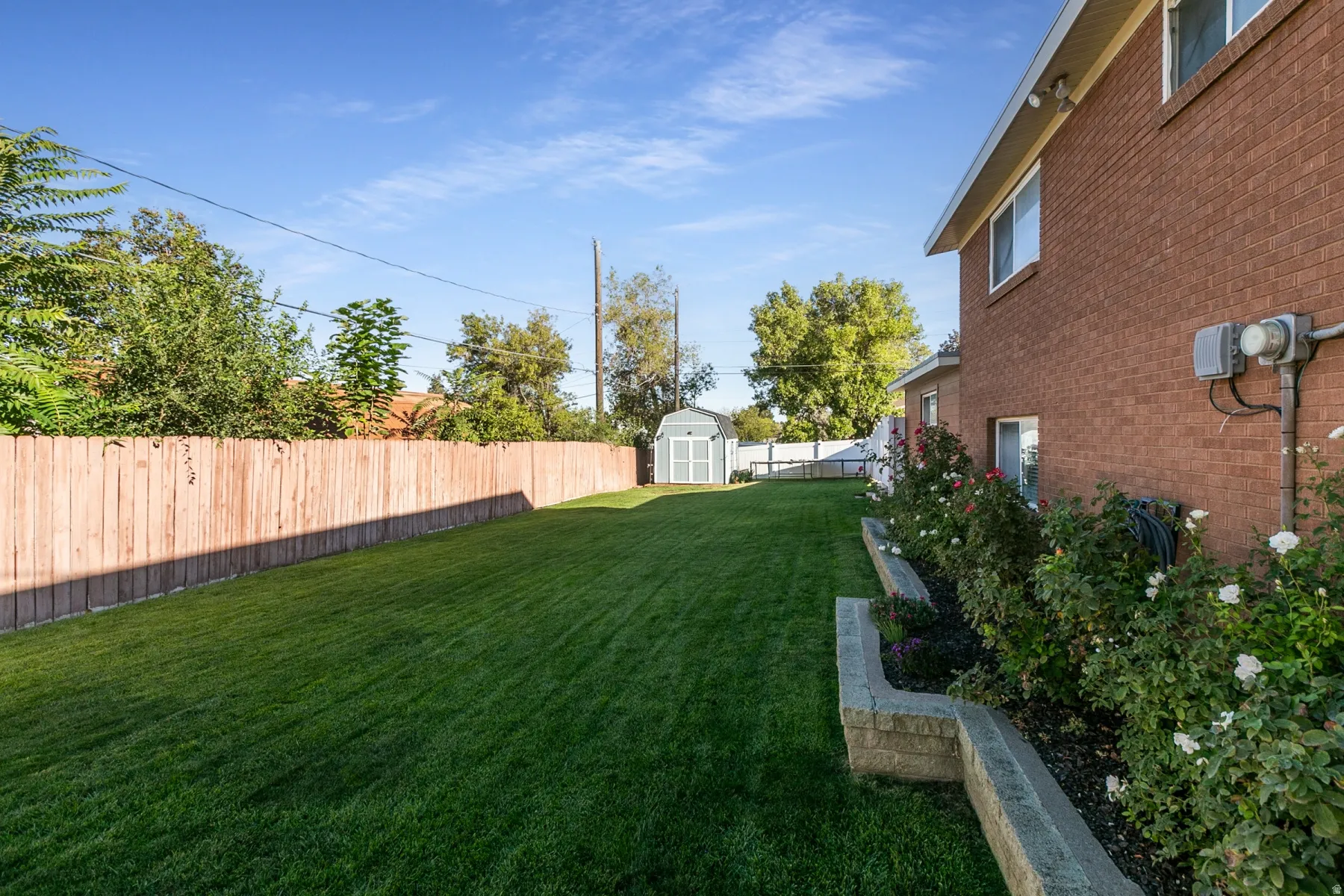 Expansive lawn area with a wood privacy fence, brick exterior, flower gardens and  storage shed