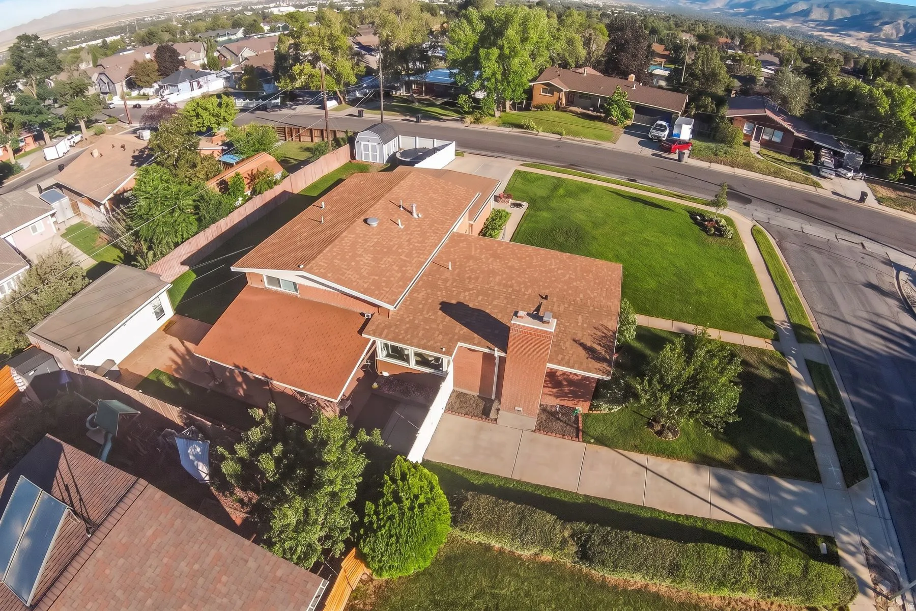 Property featuring an expansive corner lot, red shingle roofing, a brick chimney, and mature landscaping
