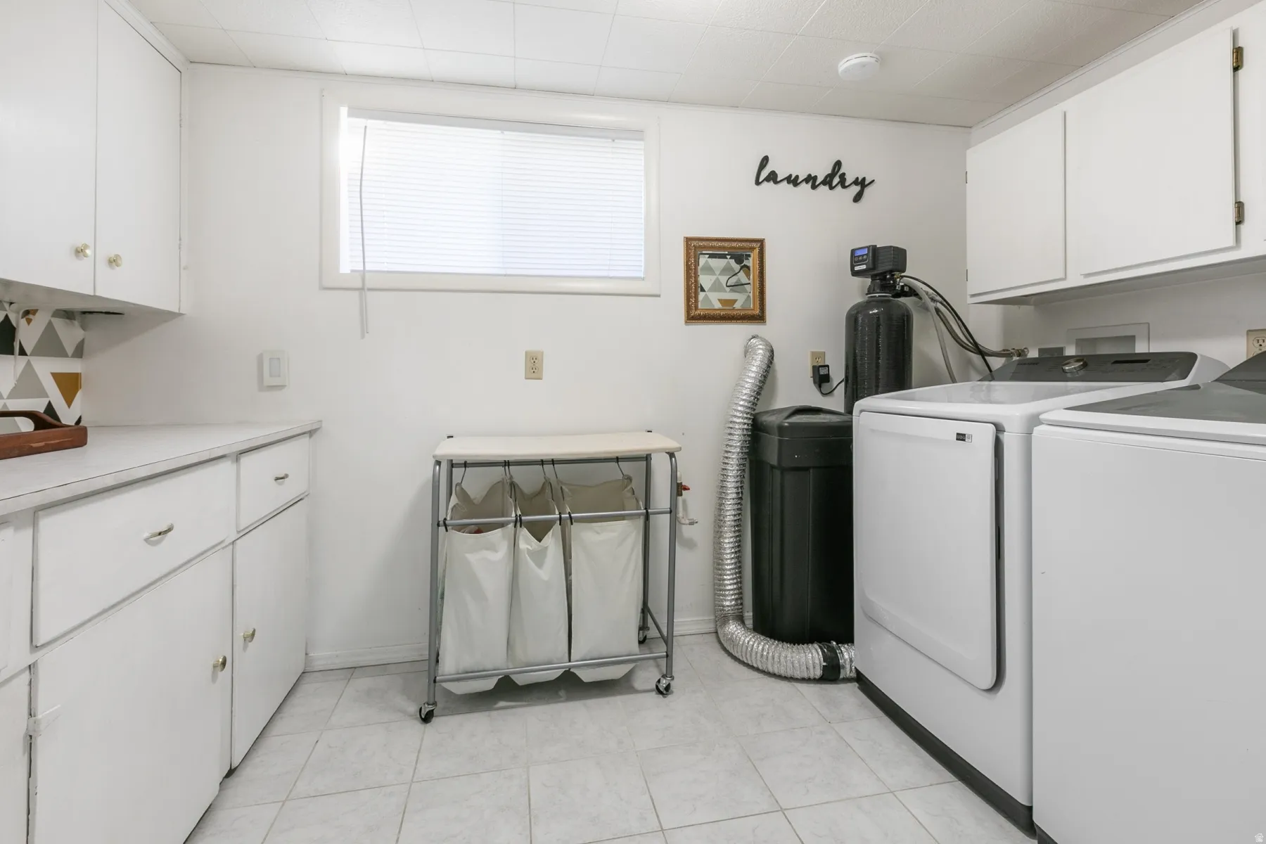 Integrated laundry area featuring white cabinetry, a window with blinds, and tiled flooring
