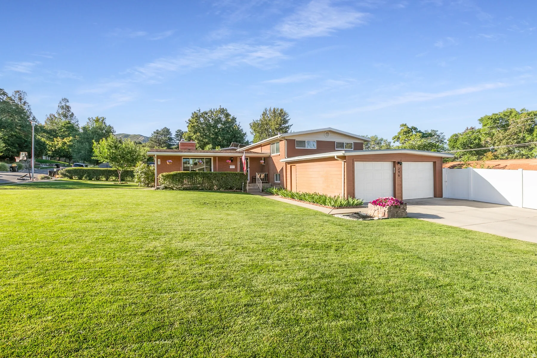 Brick exterior with a side-entry two-car garage, expansive lawn, mature landscaping, and a paved driveway