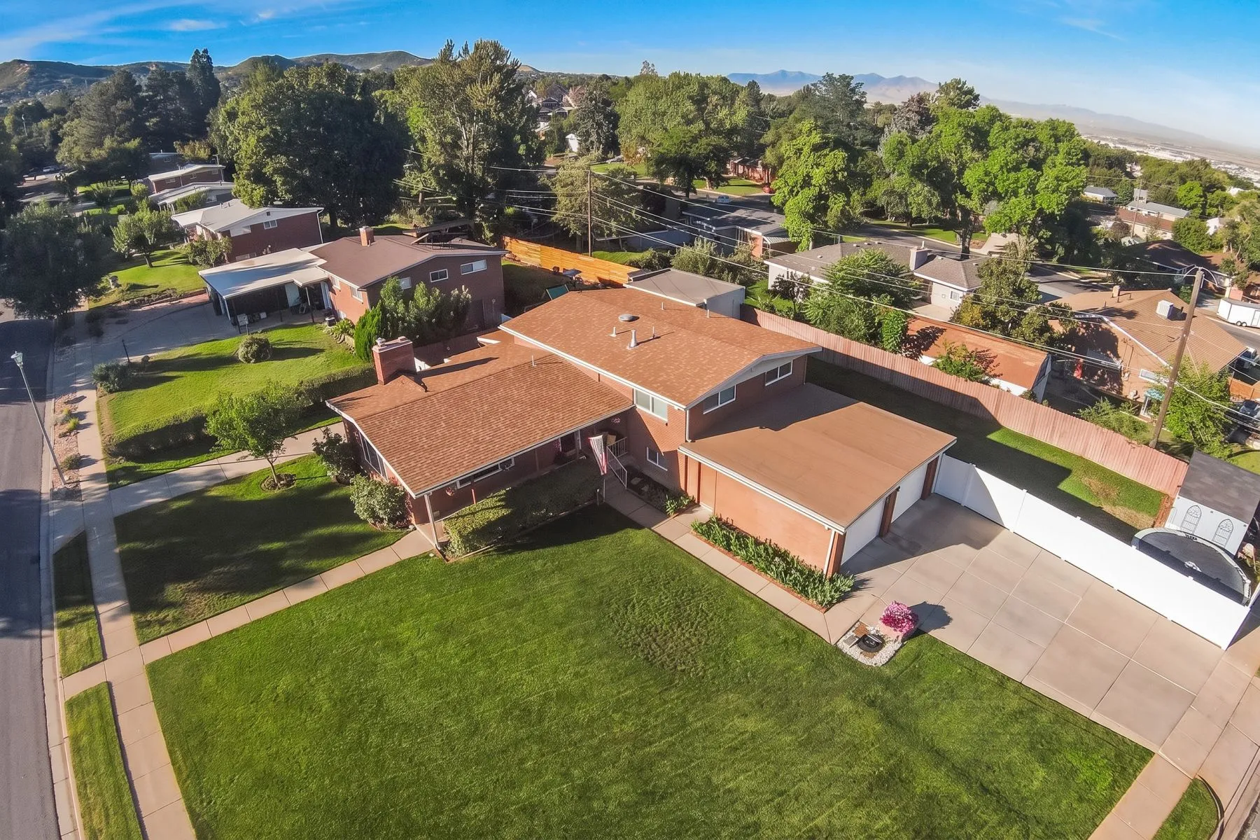 Brick exterior with a brown shingle roof, attached two-car garage, expansive front lawn, and mature perimeter trees