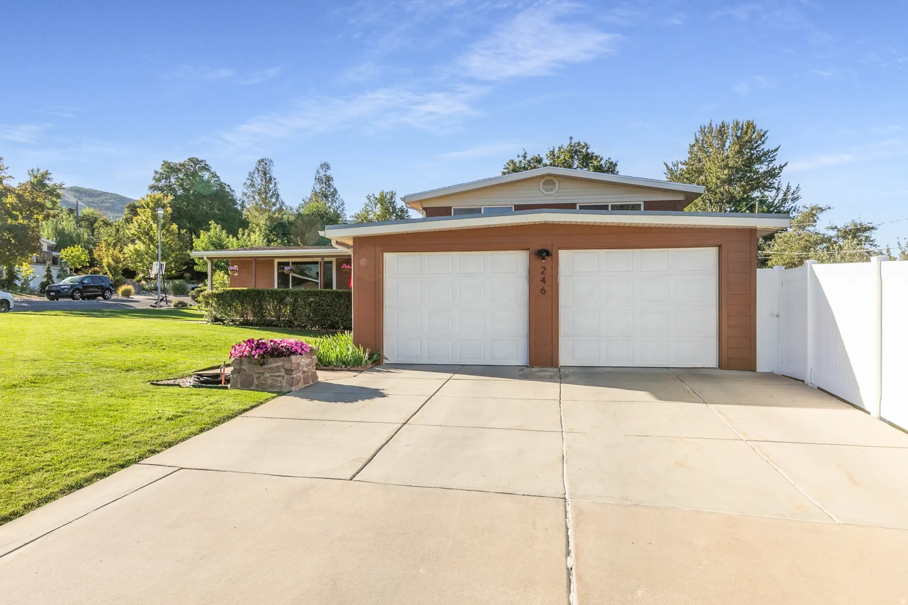 Mid-century modern exterior with a two-car attached garage, expansive concrete driveway, and a white privacy fence