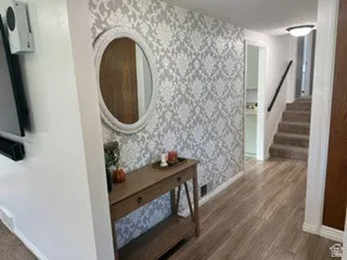 Light wood-finish flooring, patterned accent wall, staircase with carpeted treads, and ceiling-mounted flush light fixture