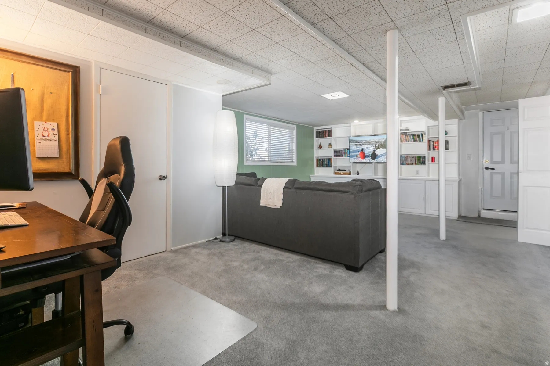 Carpeted flooring, drop ceiling, built-in shelving, white paneled doors, and a window with blinds