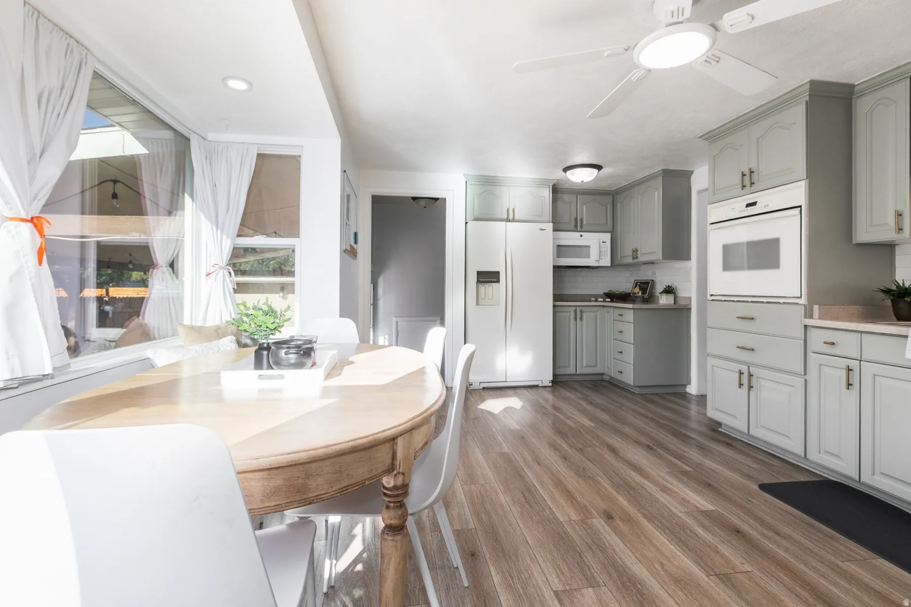 Recessed lighting, wood-finish flooring, light gray cabinetry with gold hardware, white built-in appliances, and a ceiling fan