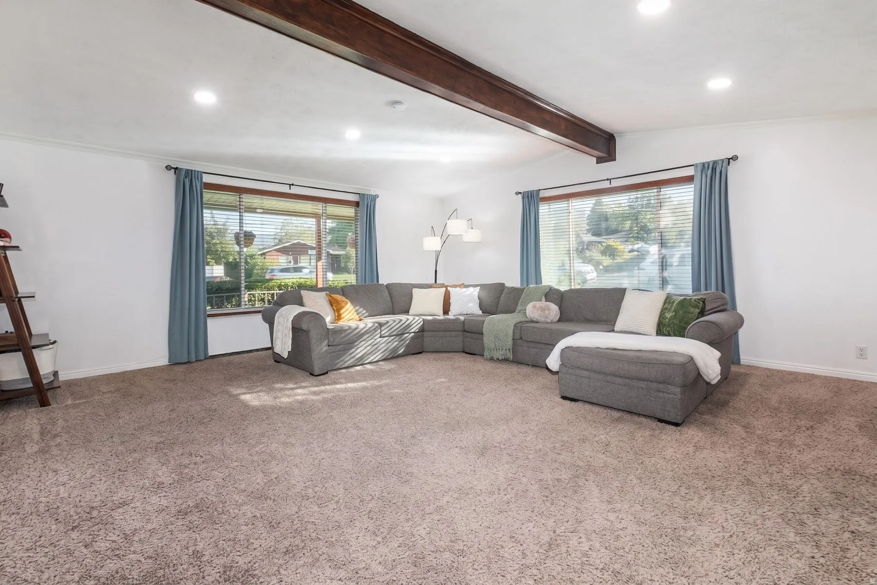 Expansive living area featuring recessed lighting, a decorative wood beam, two large windows, and neutral carpeting