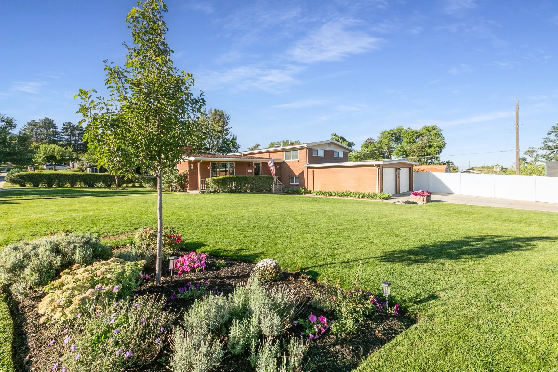 Brick exterior residence with a two-car garage, expansive lawn, and flower garden