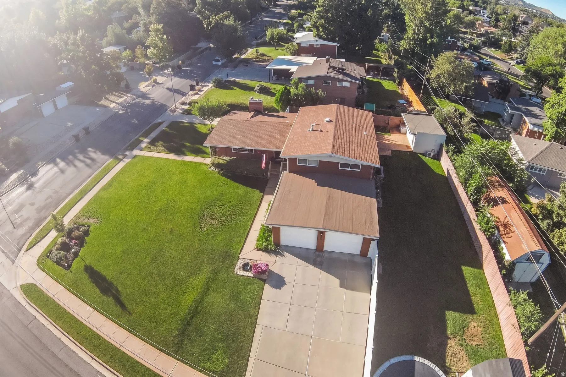 Corner lot property featuring a two-car garage, expansive front lawn, and mature perimeter trees