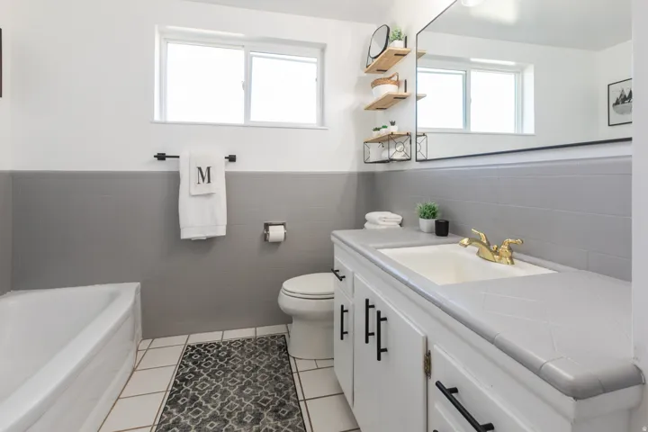 Bathroom featuring a white bathtub, toilet, vanity with integrated sink, gold-tone faucet, and a large wall-mounted mirror