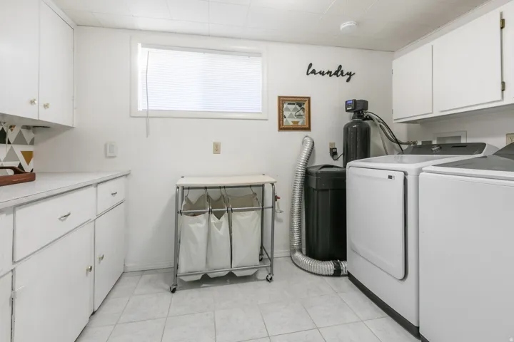 Integrated laundry area featuring white cabinetry, a window with blinds, and tiled flooring