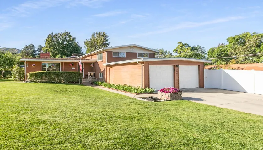 Brick exterior with white trim, attached two-car garage, concrete driveway, and expansive lawn