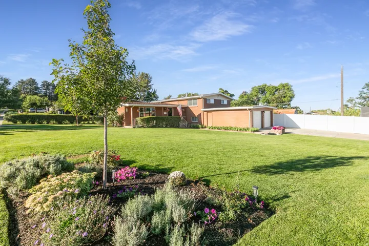 Brick exterior residence with a two-car garage, expansive lawn, and flower garden