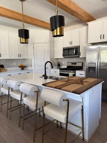 White cabinetry, chevron tile backsplash, stainless steel appliances, exposed wood beams, and a large center island with integrated sink