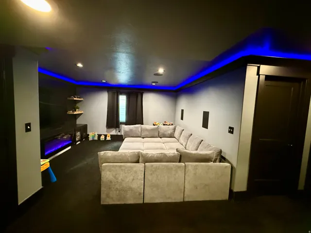 Recessed lighting, cove lighting with blue accents, dark trim, dark interior door, and wall-mounted speakers