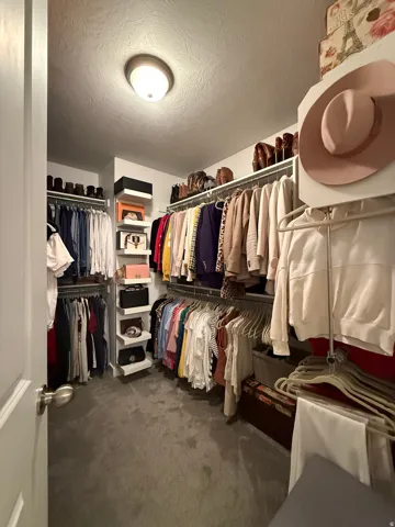 Walk-in closet with carpet flooring, built-in shelving, and multiple hanging rods for organization
