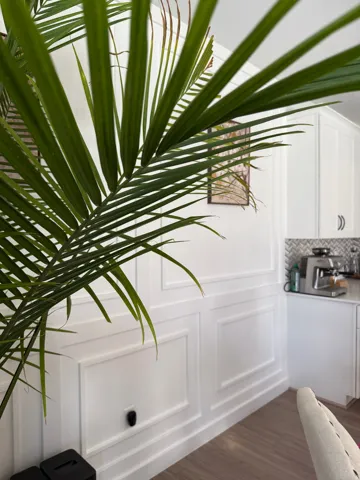 White wainscoting paneling, wood-finish flooring, white upper cabinetry, white lower cabinetry, and a patterned tile backsplash