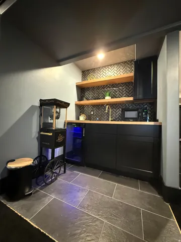 Built-in wet bar featuring dark cabinetry, wood-finish countertops, a beverage refrigerator, and open wood-finish shelving set against a herringbone tile backsplash
