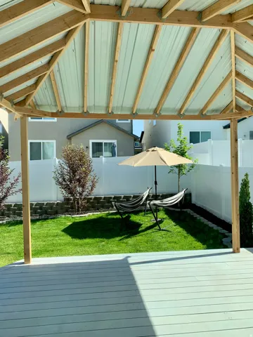 Covered patio with a light gray deck, metal roof, and exposed wood beams overlooking a manicured lawn