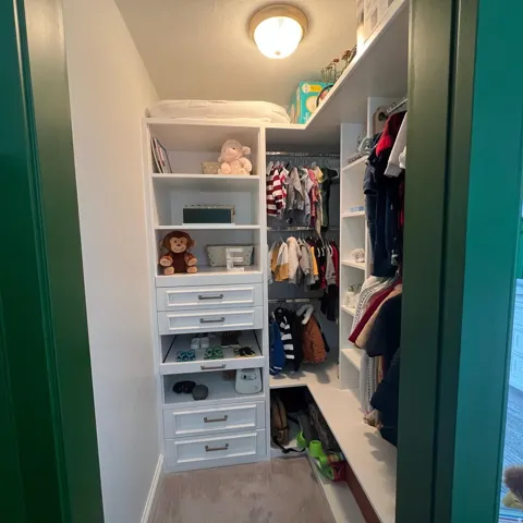 Custom closet organization system featuring white cabinetry, multiple drawers with bronze hardware, open shelving, and integrated hanging rods