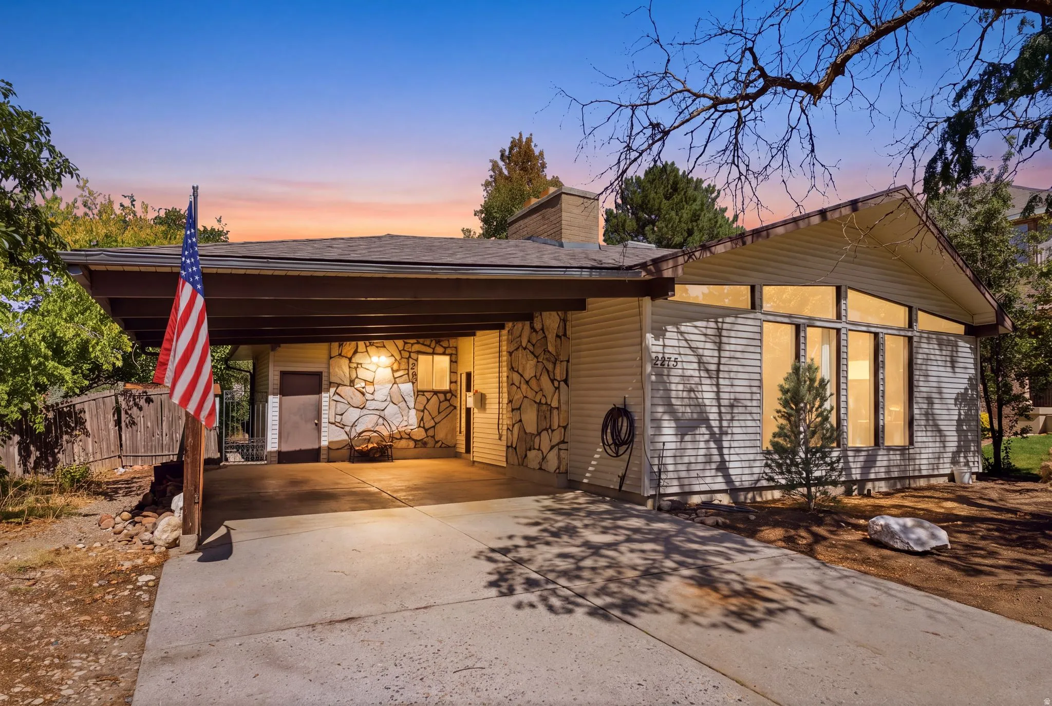 Attached carport, stone façade accents, multiple large windows, pitched roof, and a paved driveway