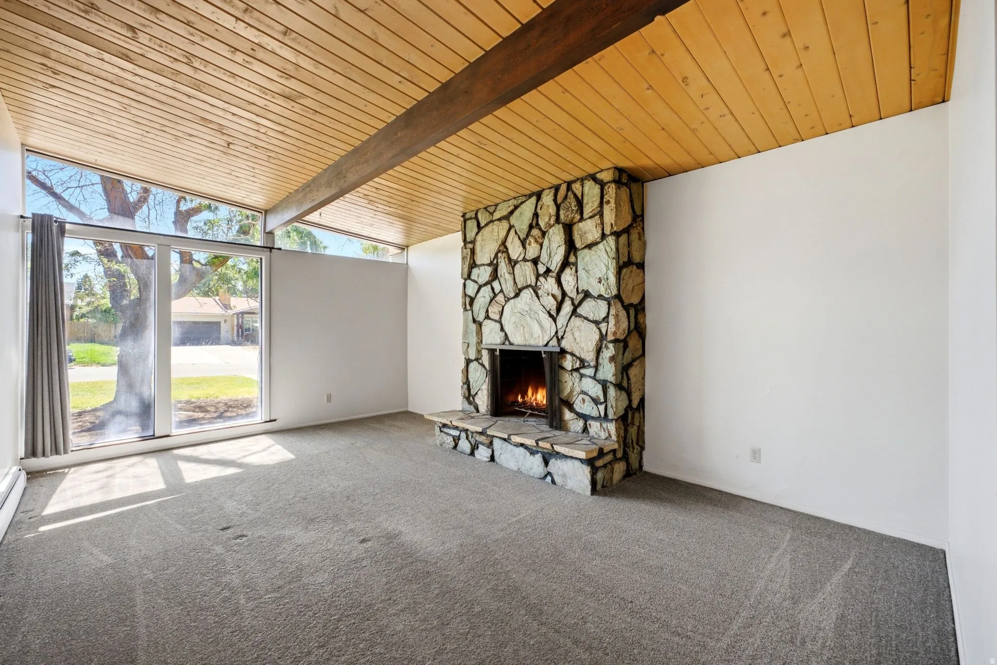 Vaulted wood-paneled ceiling with exposed beam, floor-to-ceiling windows, and a stone-clad fireplace