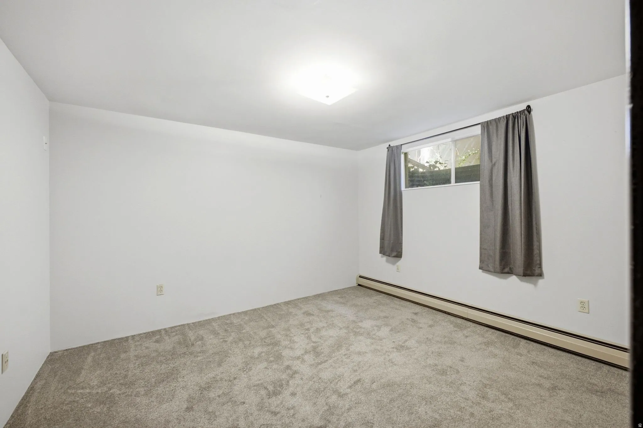 Carpeted room with a rectangular window, white walls, and a flush-mount ceiling light