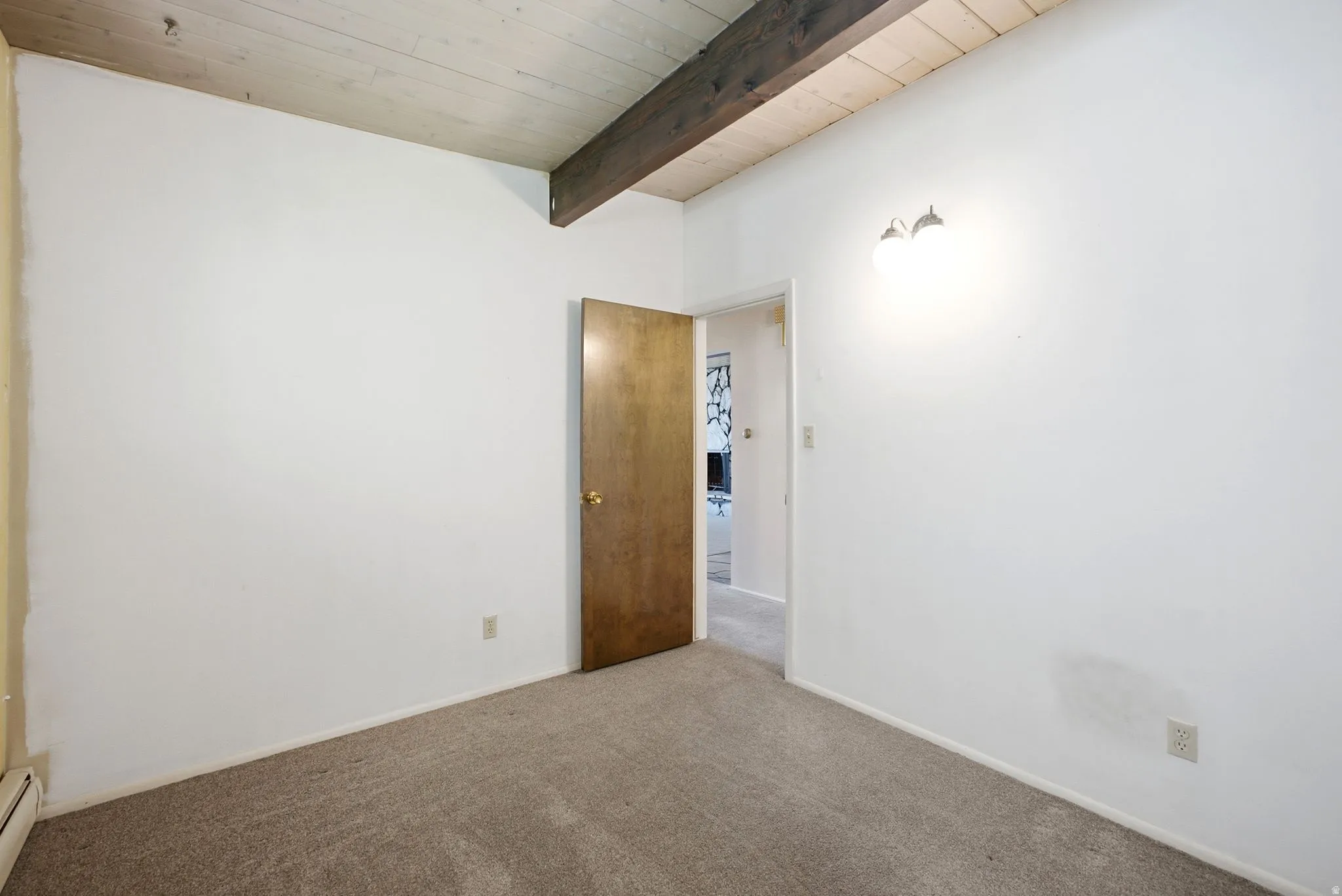 Vaulted wood-paneled ceiling with exposed wood beam, wall-mounted light fixture, and neutral carpeting