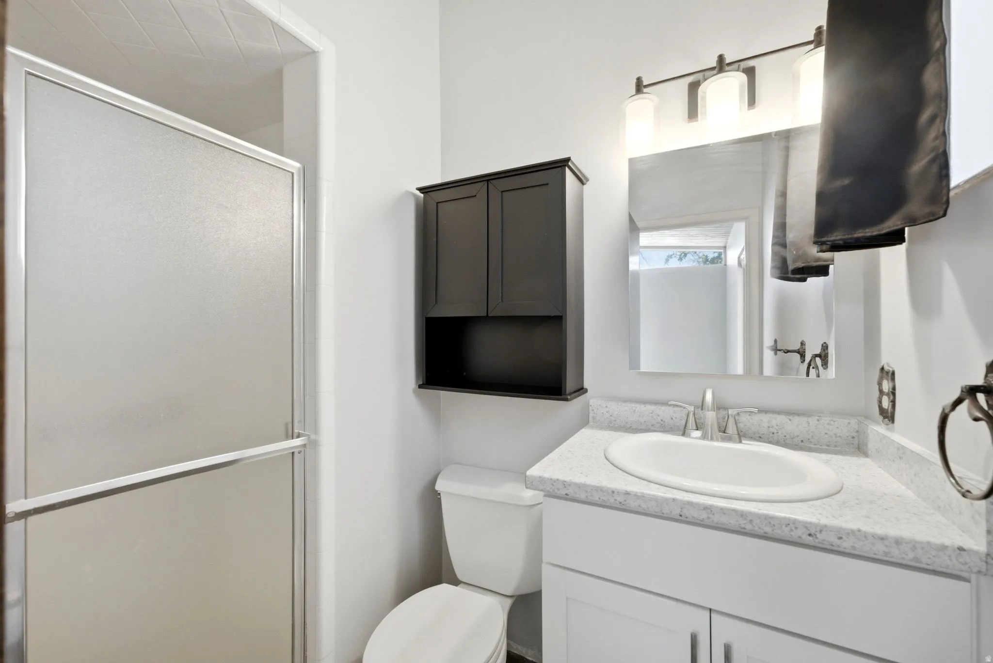 Frosted shower enclosure, vanity with speckled countertop, undermount sink, built-in medicine cabinet, and wall-mounted vanity lighting