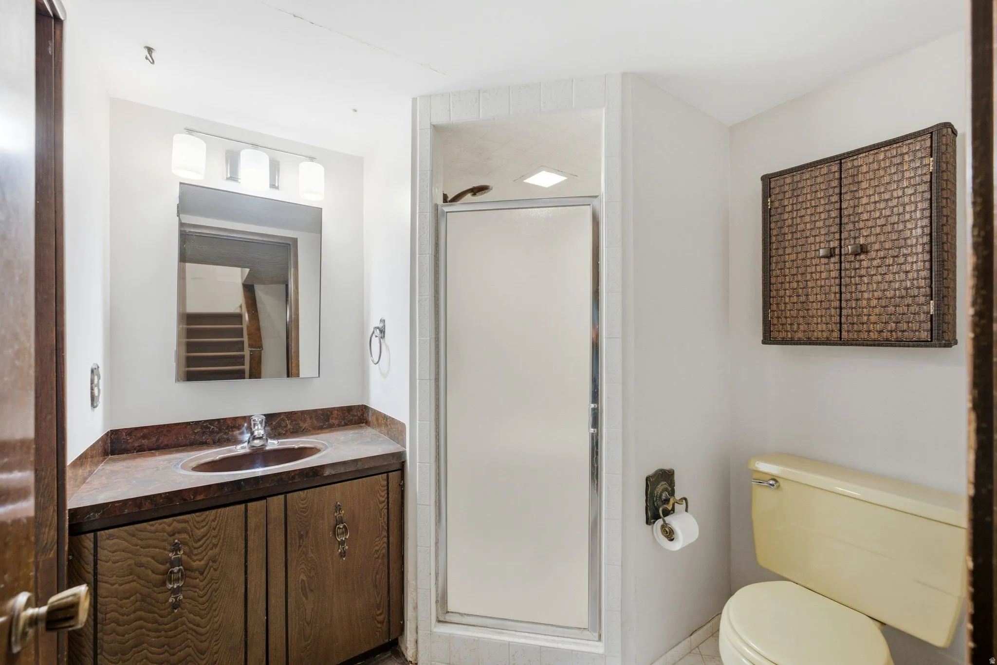 Vanity with a built-in sink, shower enclosure, wall-mounted storage cabinet, and toilet