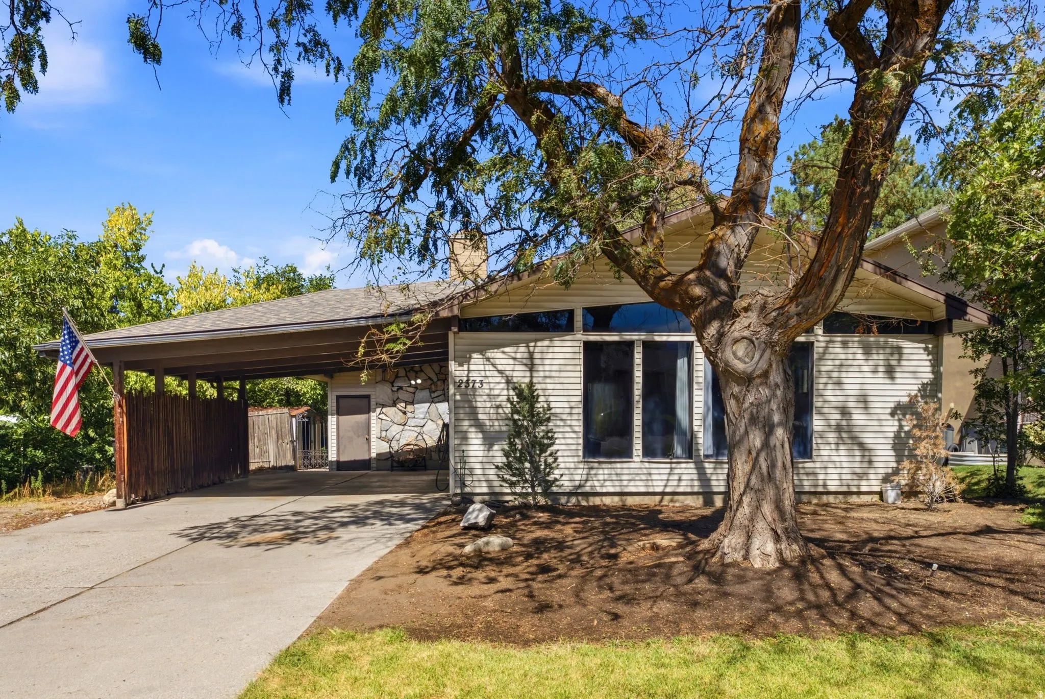 Carport with a wood fence, concrete driveway, and stone accent wall