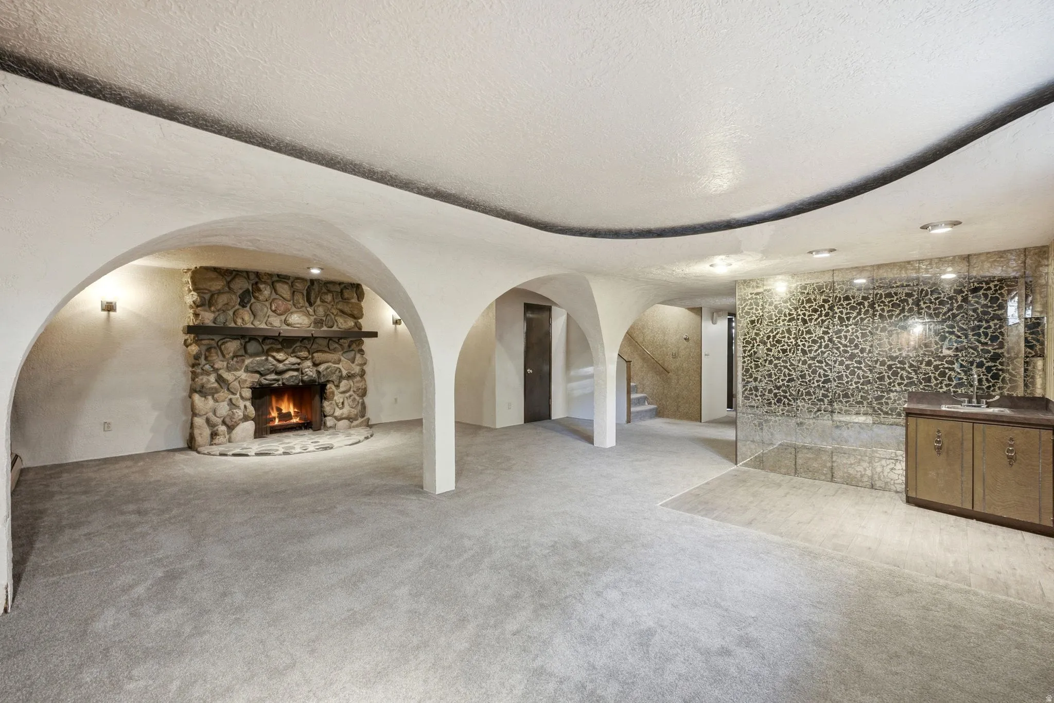 Stone fireplace with hearth, arched doorways, built-in wet bar with sink, mirrored wall accent, and recessed lighting