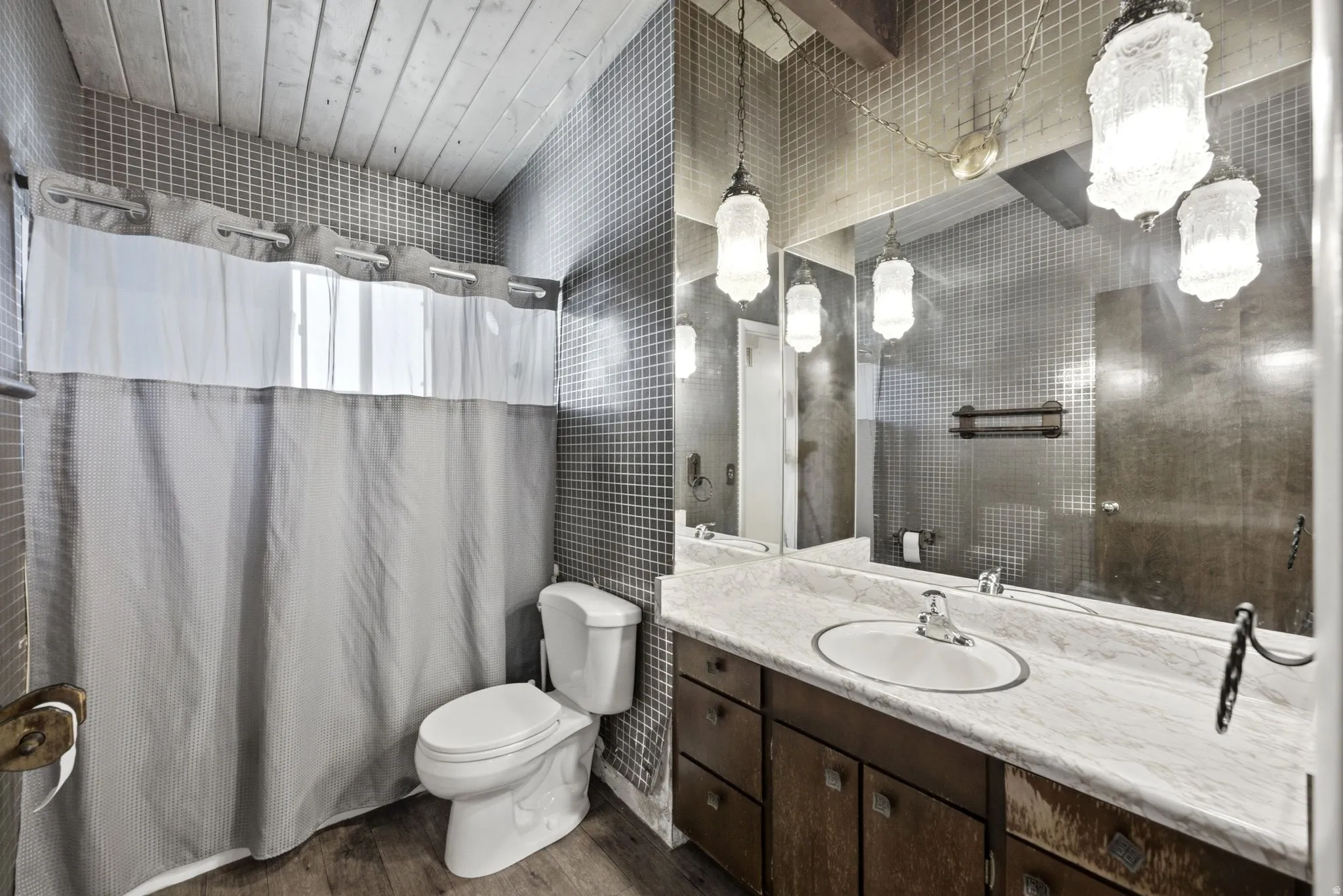 Bathroom featuring a wood-finish vaulted ceiling, full-height mosaic tile, wood-finish vanity with an integrated sink, and an expansive wall mirror