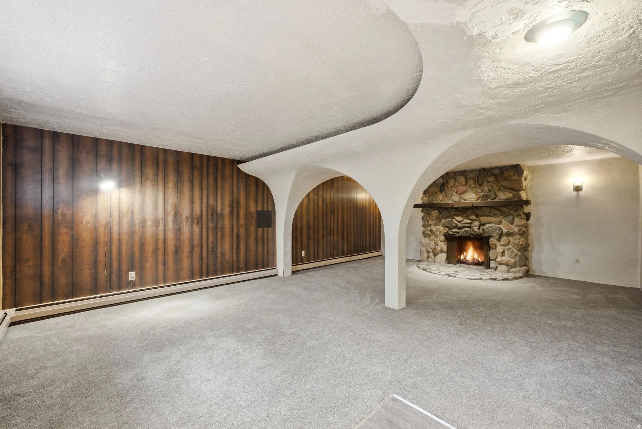 Stone fireplace with a wood mantel, wood-paneled accent wall, architectural ceiling arches, and wall sconce lighting