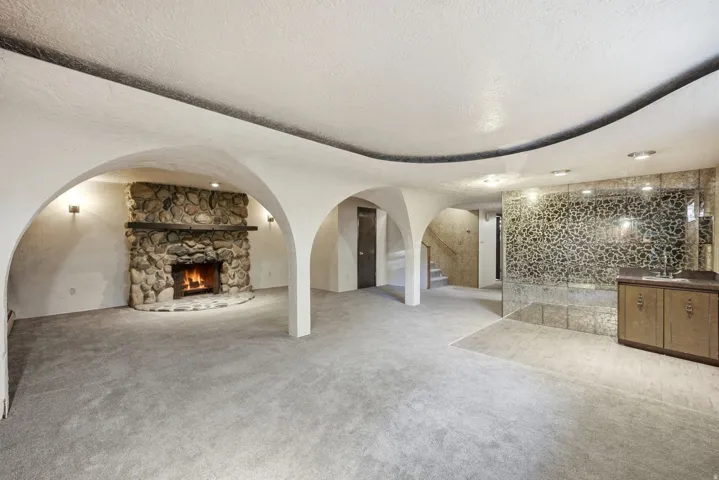 Stone fireplace with hearth, arched doorways, built-in wet bar with sink, mirrored wall accent, and recessed lighting