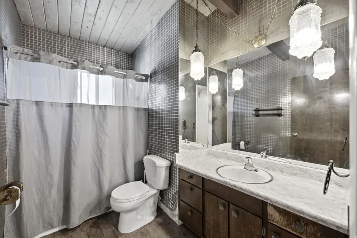 Bathroom featuring a wood-finish vaulted ceiling, full-height mosaic tile, wood-finish vanity with an integrated sink, and an expansive wall mirror