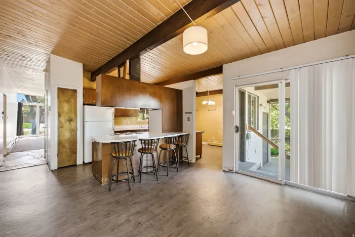 Wood-finish flooring throughout, exposed beam and wood panel ceiling, kitchen island with seating, built-in kitchen cabinetry, and sliding glass door
