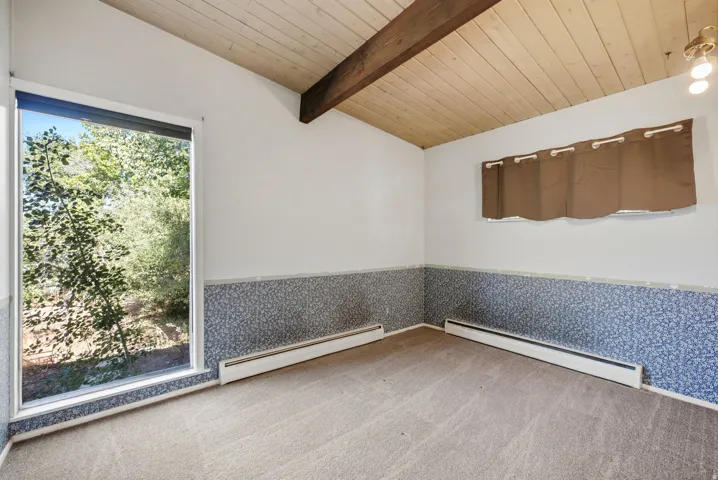 Sloped wood-plank ceiling with exposed wood beam, large picture window, and wall-to-wall carpeting