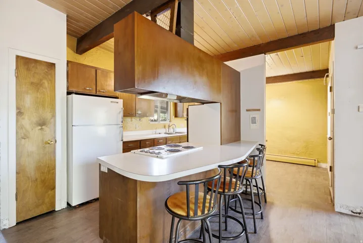 Kitchen featuring a built-in cooktop, breakfast bar, wood-finish cabinetry, wood-paneled ceiling, and exposed wood beams