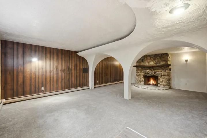Stone fireplace with a wood mantel, wood-paneled accent wall, architectural ceiling arches, and wall sconce lighting