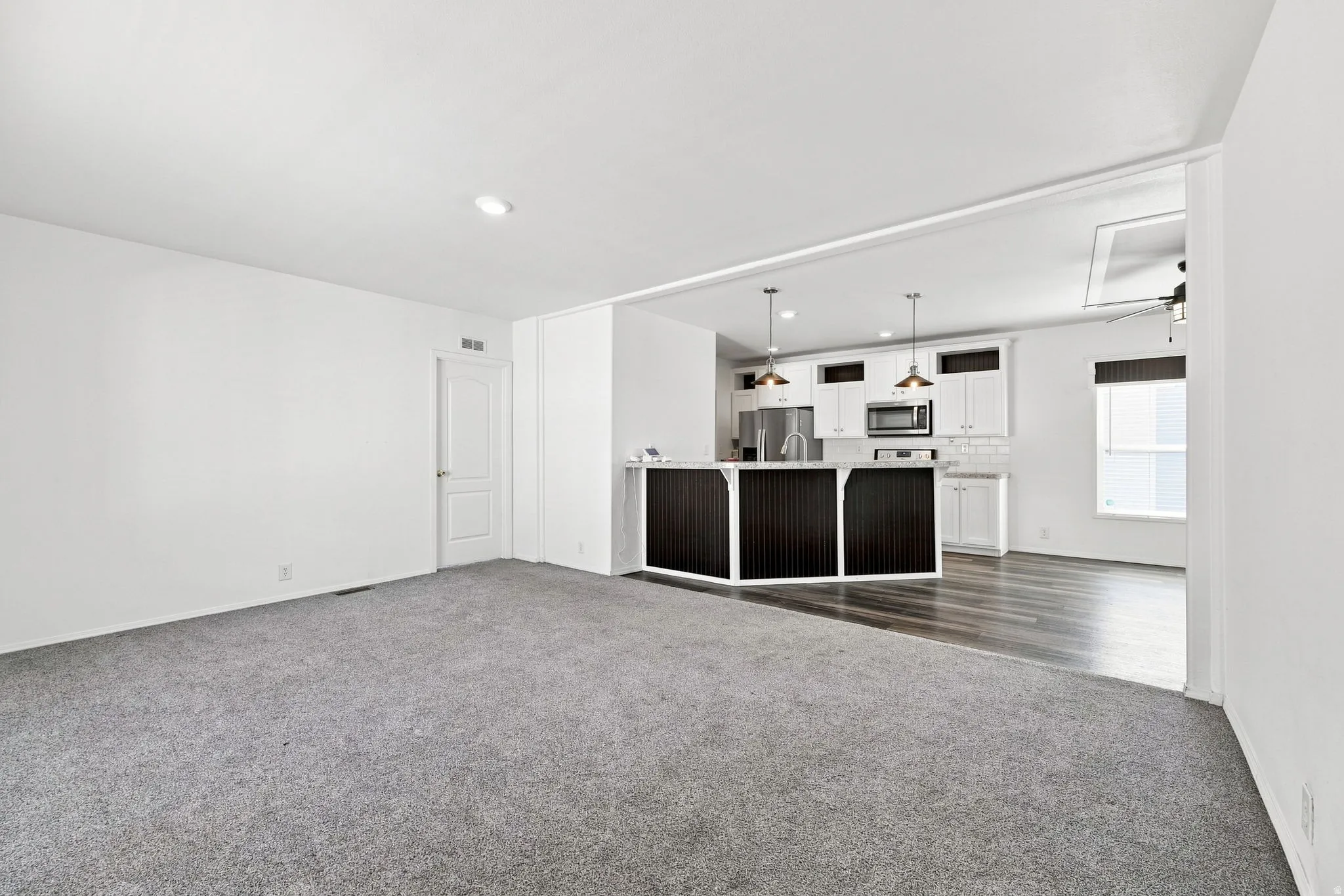 Open-concept living space with gray carpeting, white walls, and recessed lighting