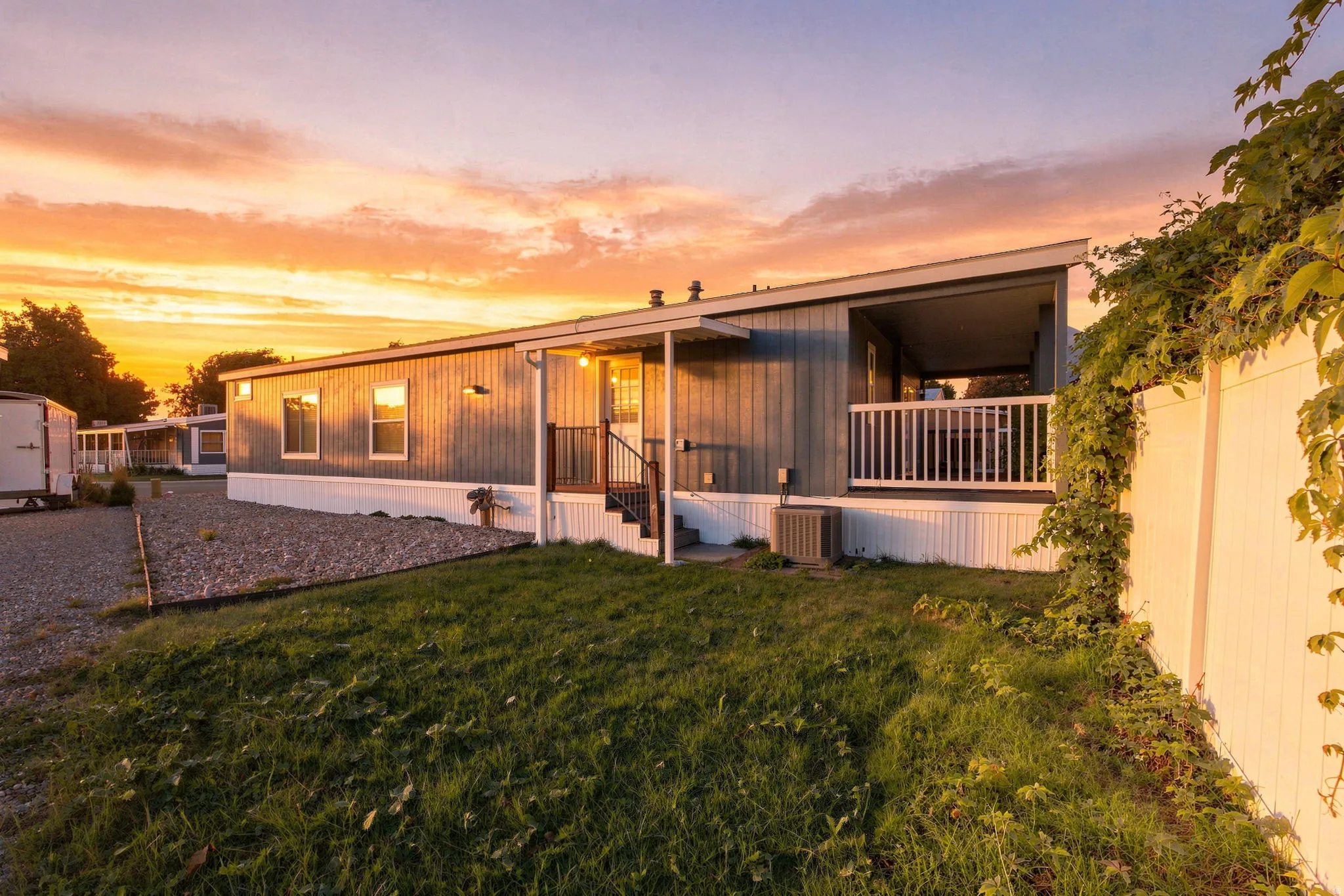 Modern manufactured home with metal exterior siding and expansive covered front porch featuring white railings