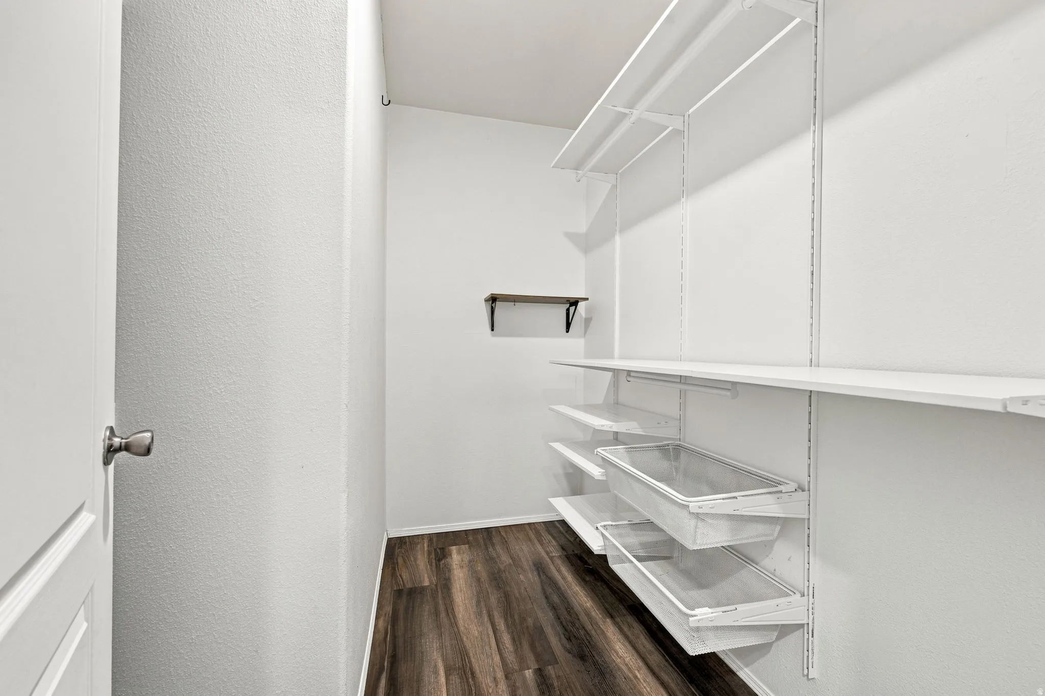 Wood-finish flooring, white walls, built-in shelving system, sliding storage bins, and a wall-mounted floating shelf
