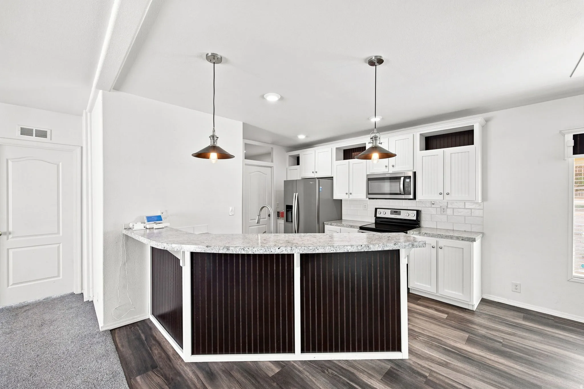 Modern kitchen featuring a breakfast bar with pendant lighting, white cabinetry, integrated stainless steel appliances, and wood-finish flooring