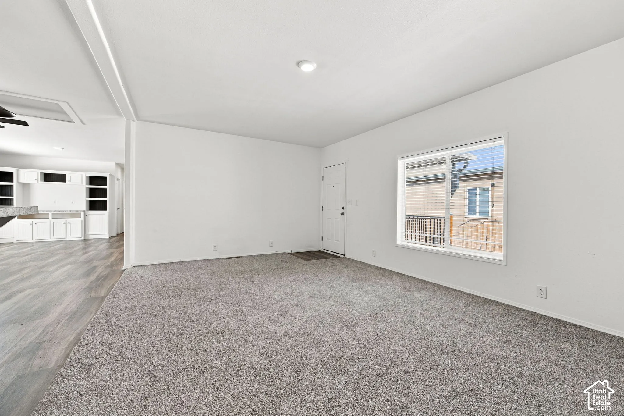 Spacious living area with grey carpeting, white walls, recessed lighting, and a front entry door