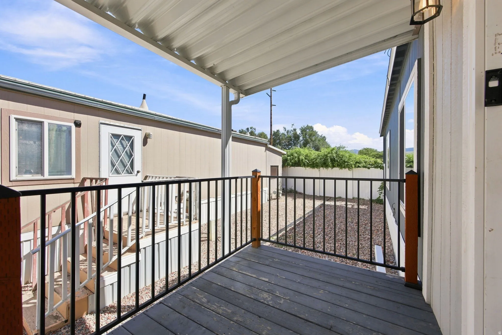 Covered outdoor deck with dark wood-finish flooring, black metal railing, and a mounted exterior light fixture