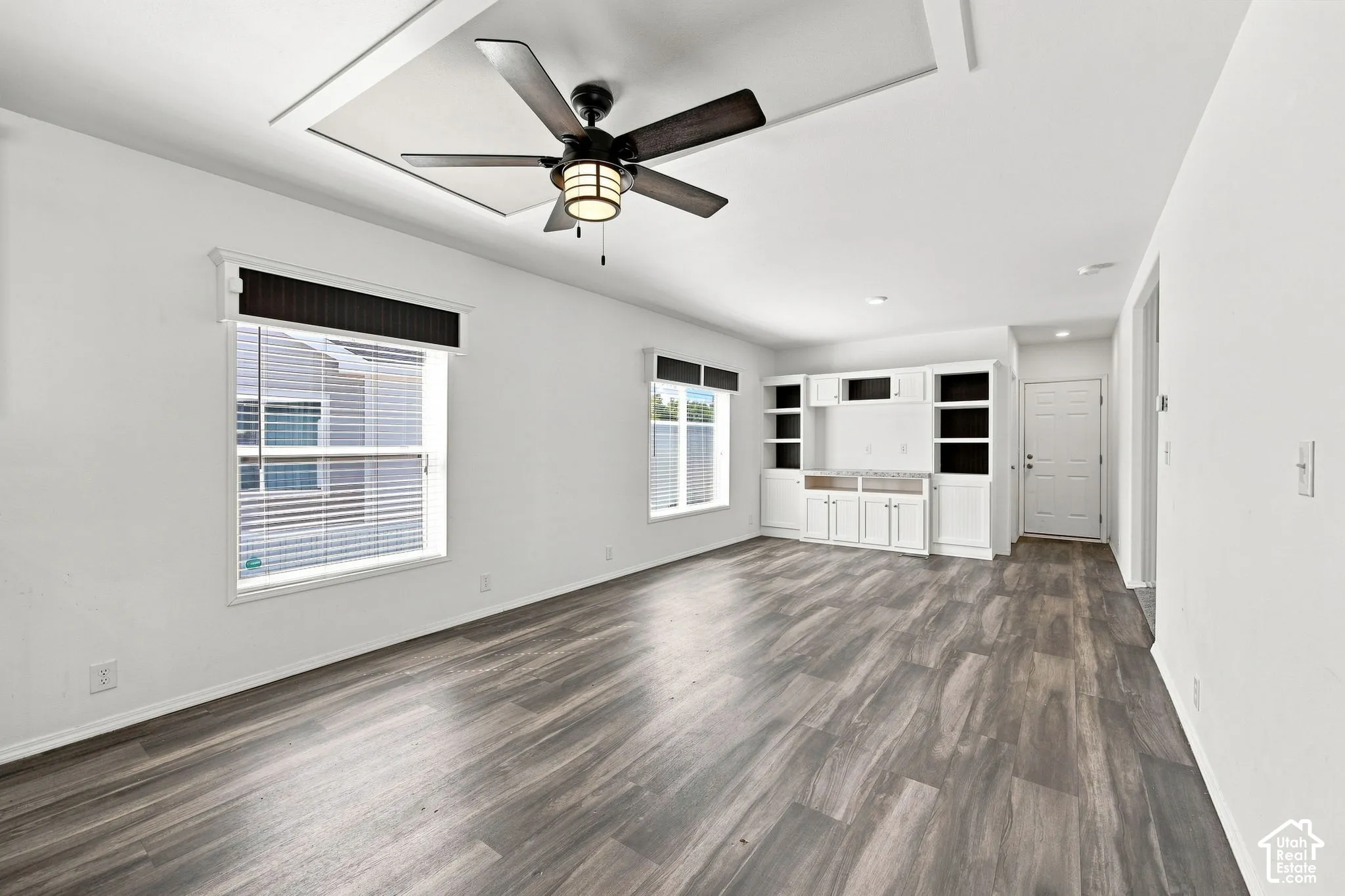 Wood-finish flooring, recessed ceiling detail, ceiling fan with integrated lighting, built-in cabinetry, and crisp white walls