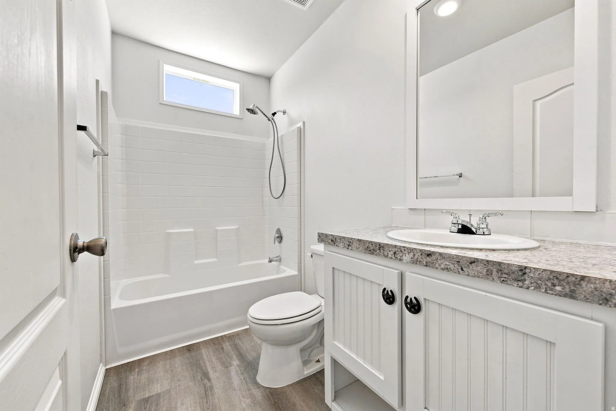 Spa-inspired bathroom featuring a frameless glass-enclosed shower with subway tile surround, dual vanity with quartz countertop and brushed nickel hardware, porcelain toilet, and wood-finish flooring throughout