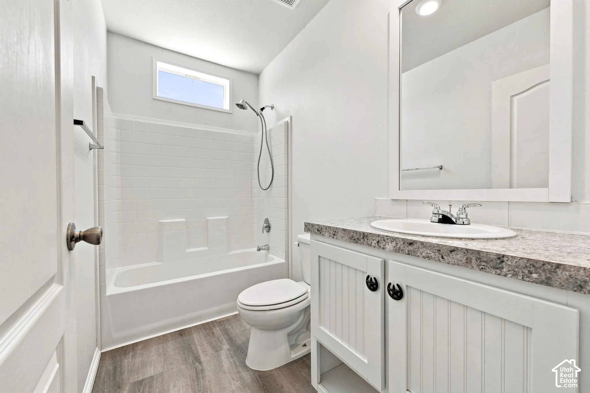 Spa-inspired bathroom featuring a frameless glass-enclosed shower with subway tile surround, dual vanity with quartz countertop and brushed nickel hardware, porcelain toilet, and wood-finish flooring throughout
