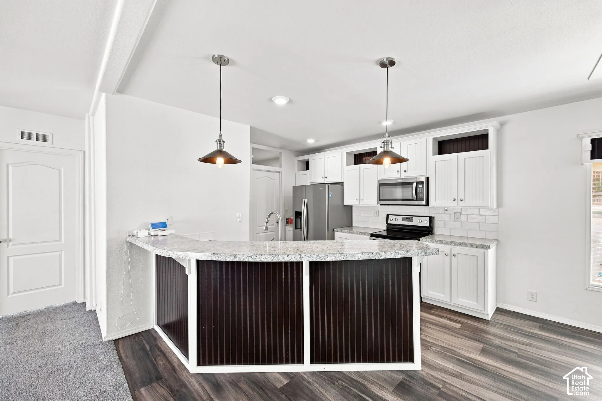 Modern kitchen featuring a breakfast bar with pendant lighting, white cabinetry, integrated stainless steel appliances, and wood-finish flooring